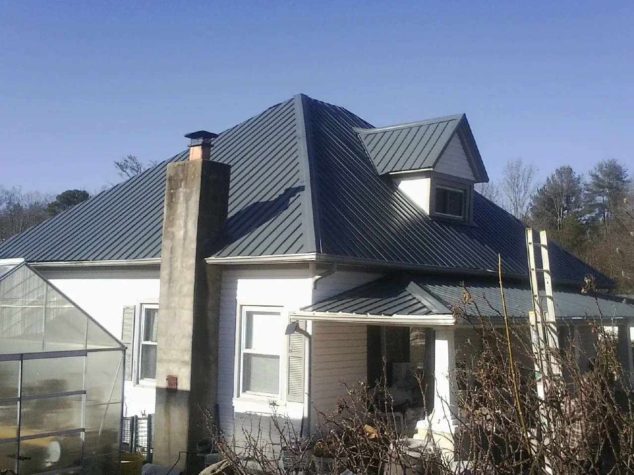 Dark blue standing seam metal roof on a white farmhouse with dormer — Slate & Tile Roof Repair by Roofing Brothers in Maxbass