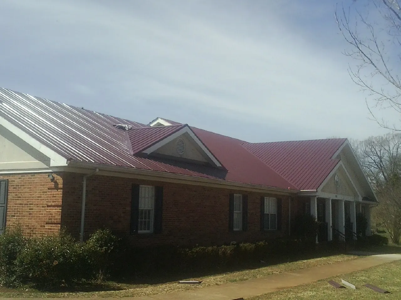Red metal roof with gabled entries on a long brick building, from a Hail Damage Roof Repair job in Maxbass