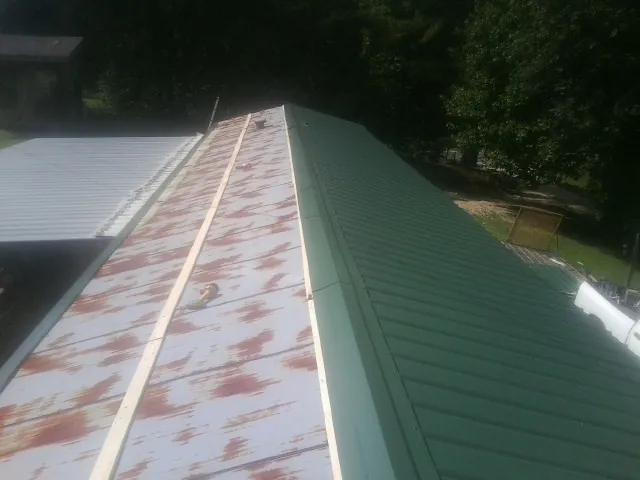 Old rusted panels beside newly installed green metal roofing — Wind Damage Roof Repair by Roofing Brothers in Maxbass