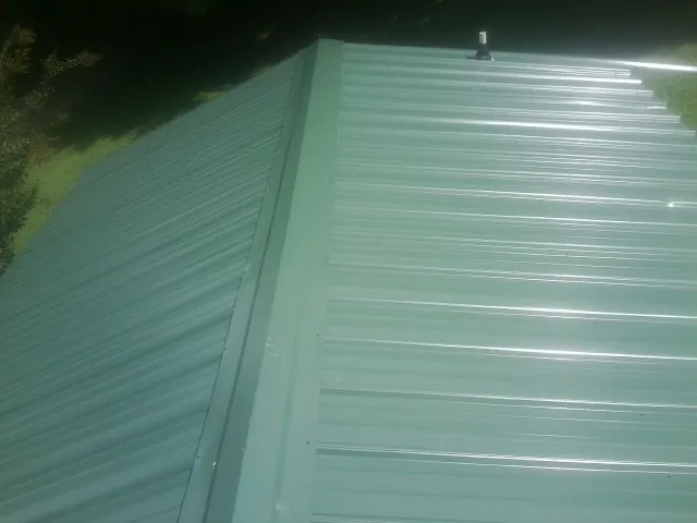 New green metal panels meeting at the ridge of a roof — Flat Roof Repair work by our crew in Maxbass