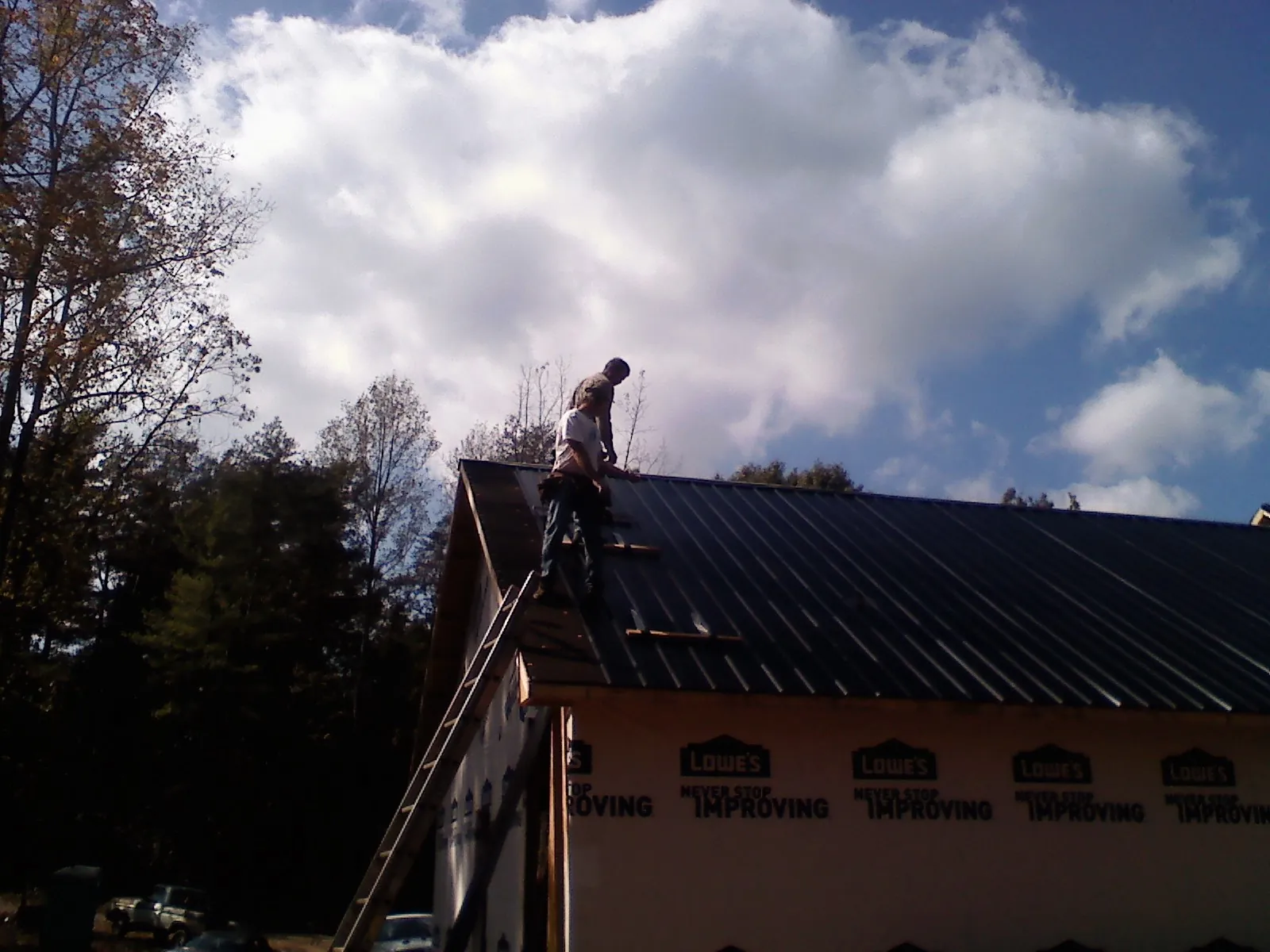 Roofer fastening dark metal panels high against a cloudy sky, from a Roof Inspection job in Maxbass
