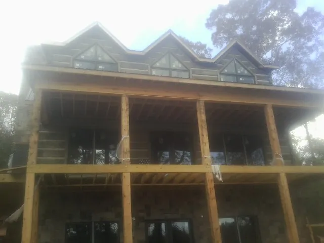 Dormers and porch framing on a large log home under construction — Roof Coating work by our crew in Maxbass