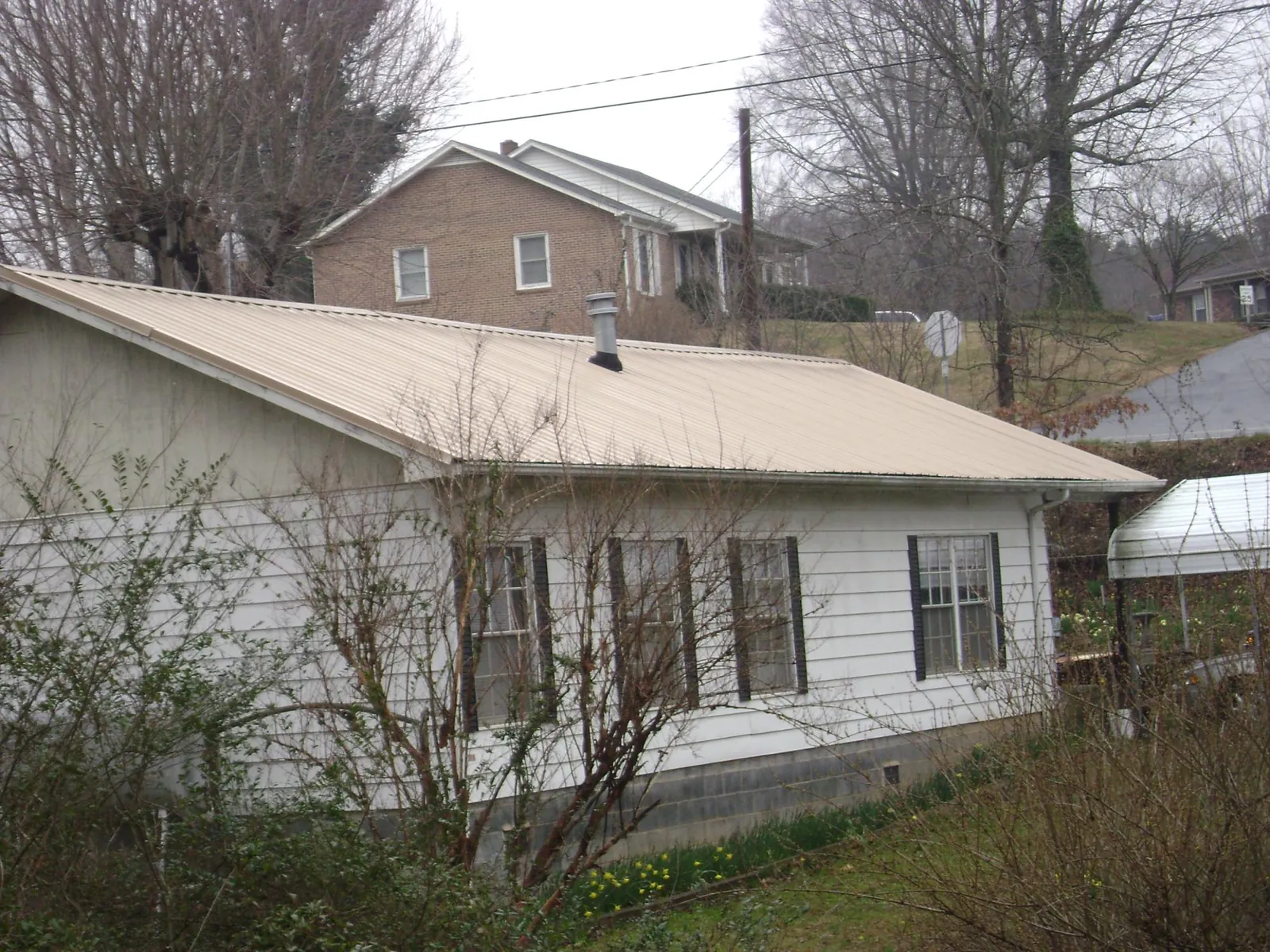 Tan metal roof on a white sided house set into a hillside — Commercial Roofing by Roofing Brothers in Maxbass