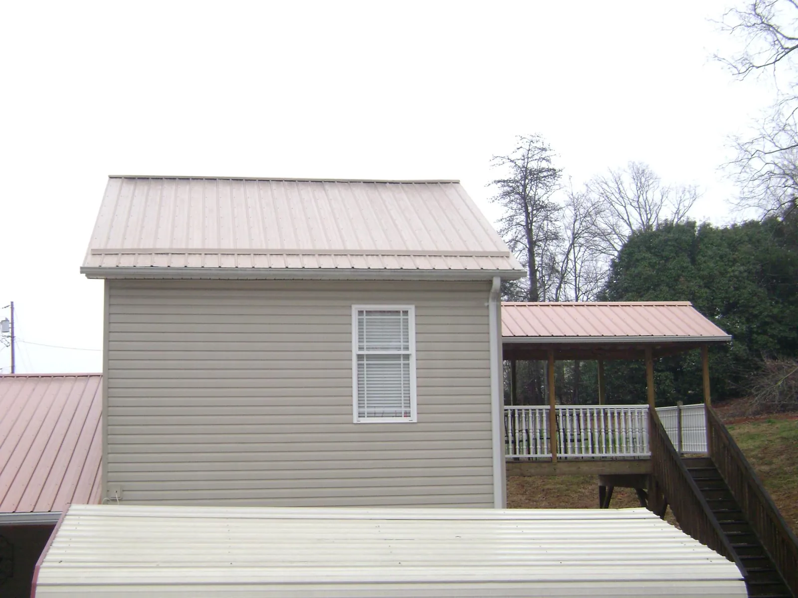 Tan metal roofs on a two story addition and attached porch, from a Roof Replacement job in Maxbass